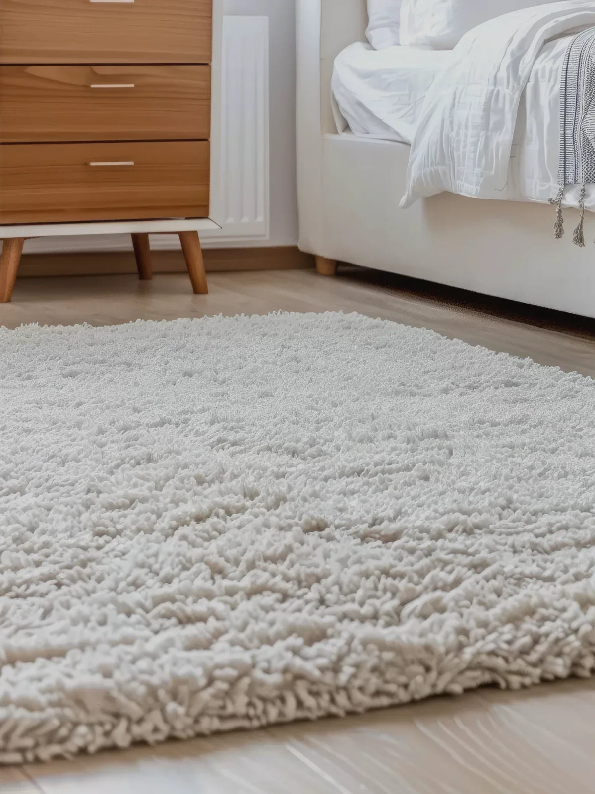 Cozy bedroom featuring a soft, plush white shag rug, adding warmth and comfort to a modern minimalist space with wooden furniture and neutral tones.