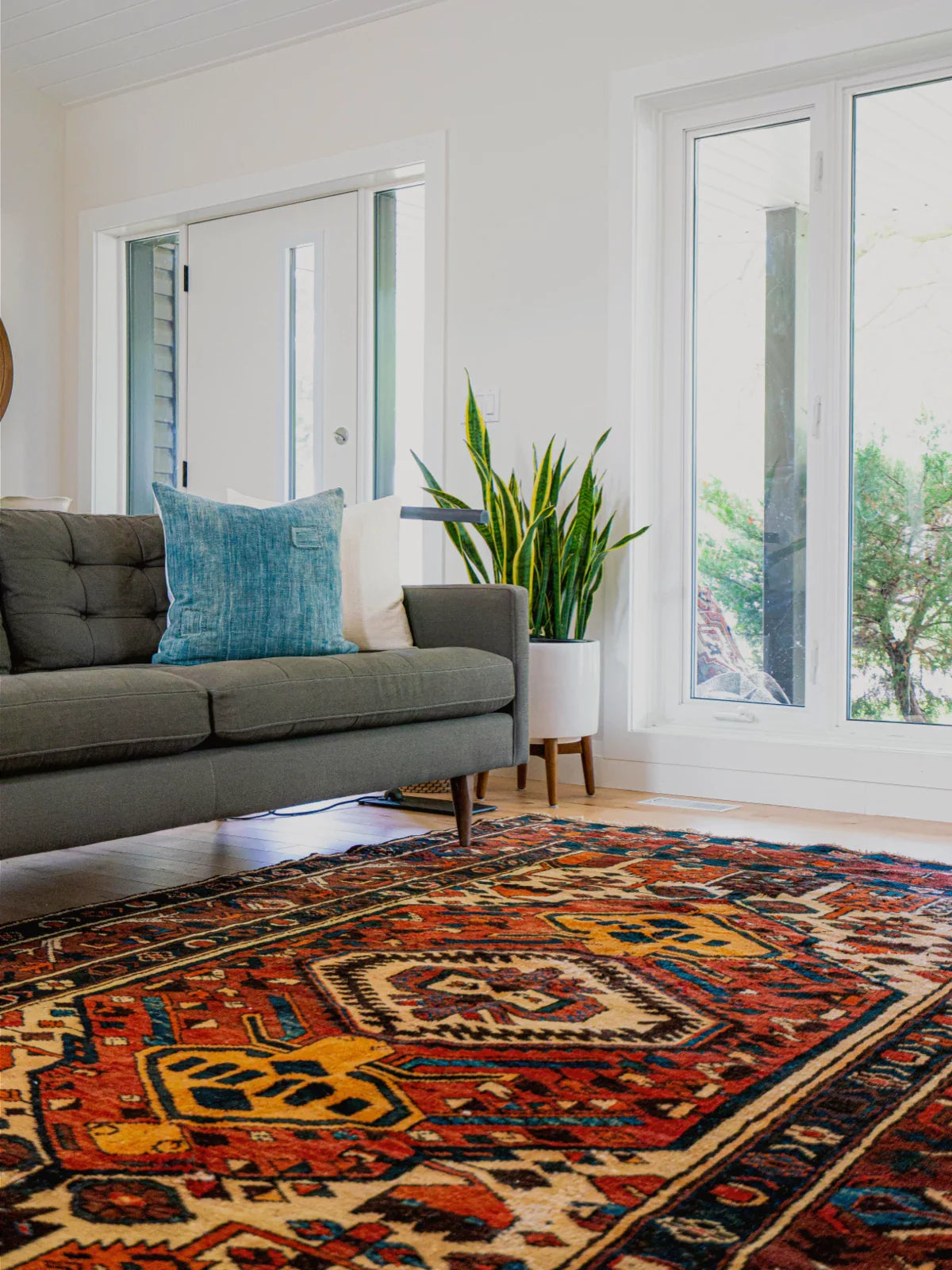 Cozy living room featuring a richly colored vintage rug with intricate geometric patterns, paired with a mid-century modern sofa and natural light-filled decor.