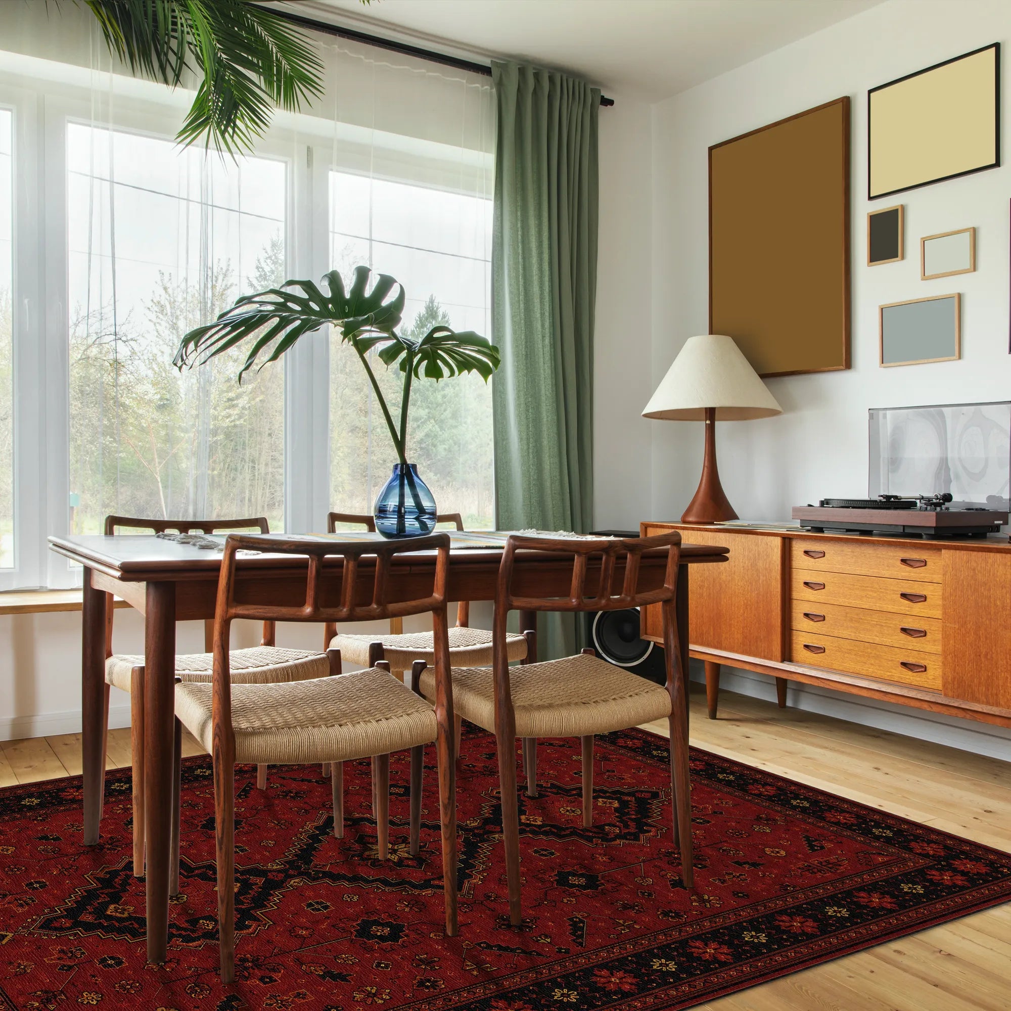 Una sala da pranzo in stile mid-century modern con un tavolo da pranzo in legno e quattro sedie con schienale intrecciato su un tappeto rosso a motivo. La stanza ha un pavimento in legno chiaro, una credenza in legno con una lampada e un giradischi, e una grande finestra con tende verdi.