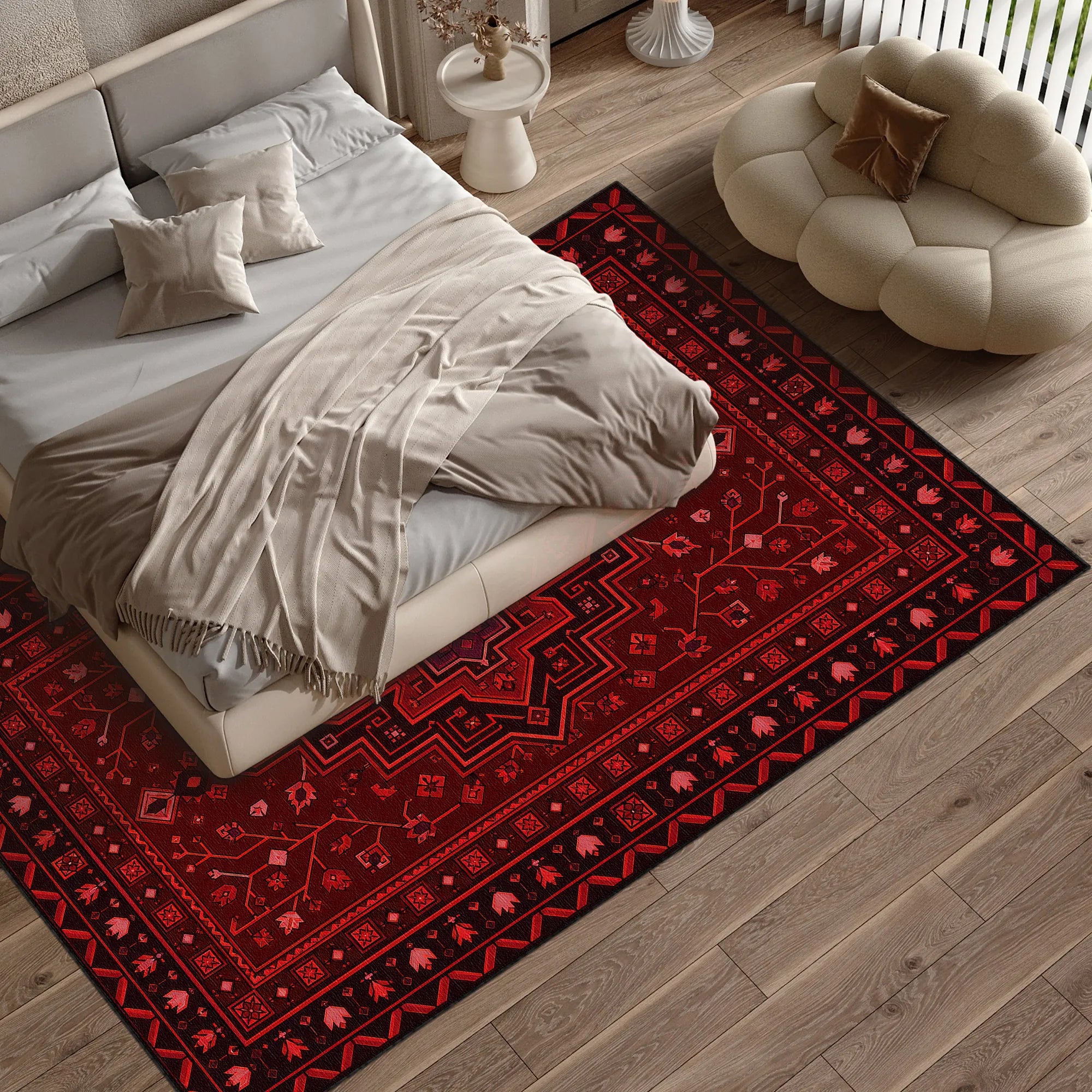A red and black patterned area rug styled on a light wood floor next to a bed with beige bedding and a cream cloud-shaped pouf in a modern bedroom setting.